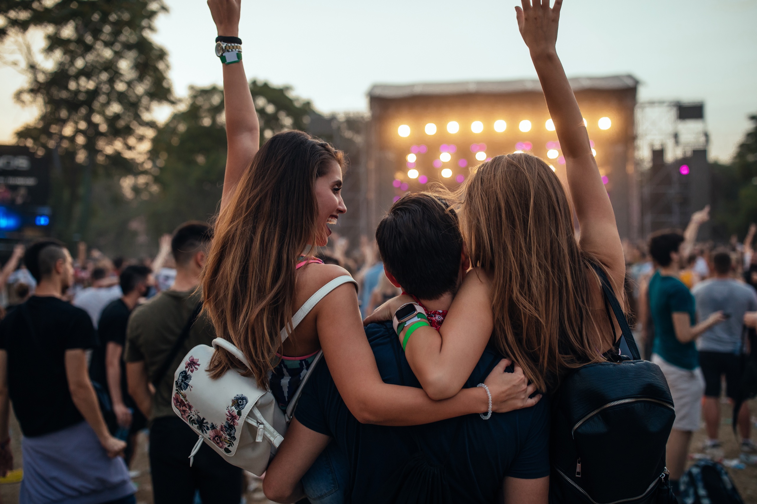 Three friends embracing in front of an outdoor music festival stage